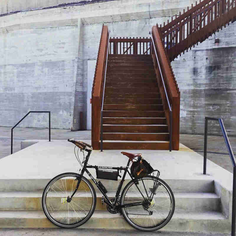 Left side view of a black Surly bike with seat & frame packs, parked in front of a staircase with a concrete wall behind