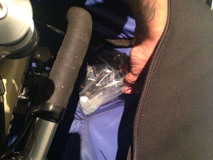 Downward view of a hand, packing a plastic bag with bike pedals and skewers, into a bike carrier bag