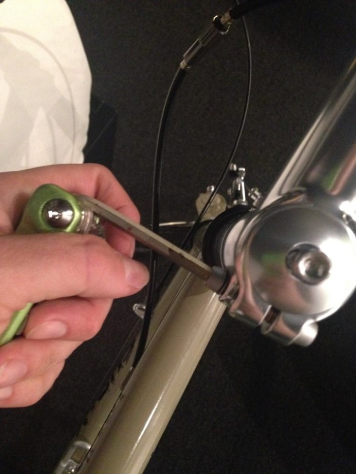 Downward, cropped view of a hand holding a hex wrench tool, removing the side bolt of a handlebar stem, on a bike