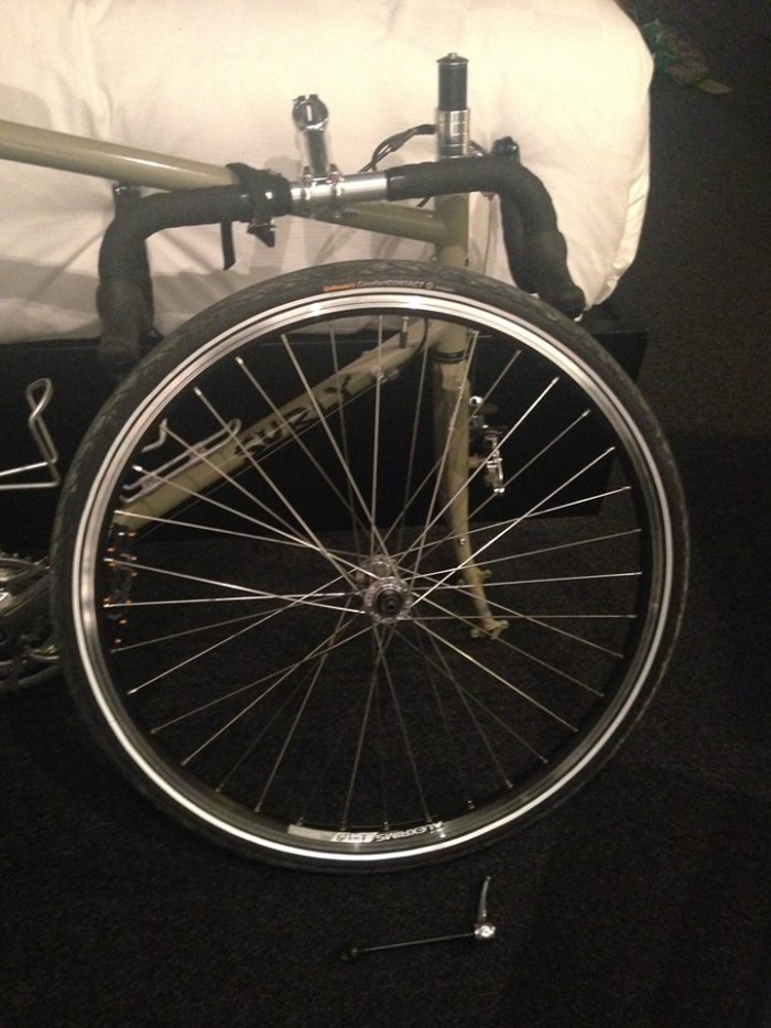 A removed front wheel of a tan Surly Long Haul Trucker bike, in front of the frame with parts