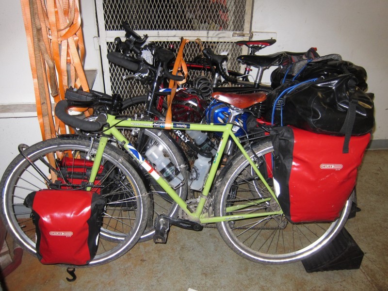 Left side view of a lime green Surly bike with gear, with other bikes behind, on a cement slab in front of a mesh door