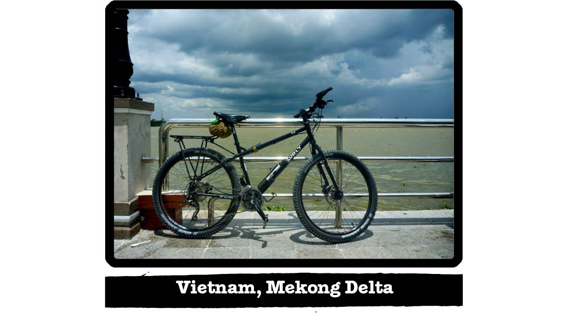 Right view of a Surly bike, black, against a steel rail on a walkway near sand - Vietnam, Mekong Delta tag below image