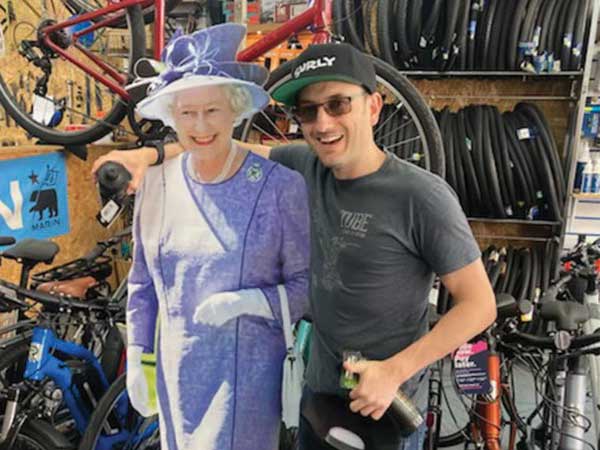 Matt in bike shop with arm around cutout of the Queen