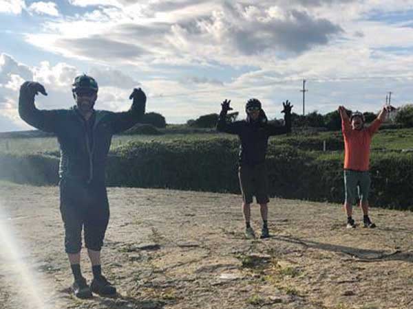 Three cyclist with arms up standing on rock slab with dinosaur prints