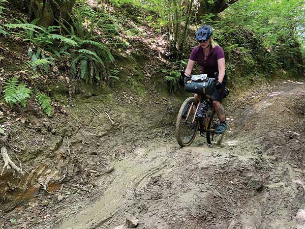 Lone cyclist riding loaded bike up very muddy forest trail