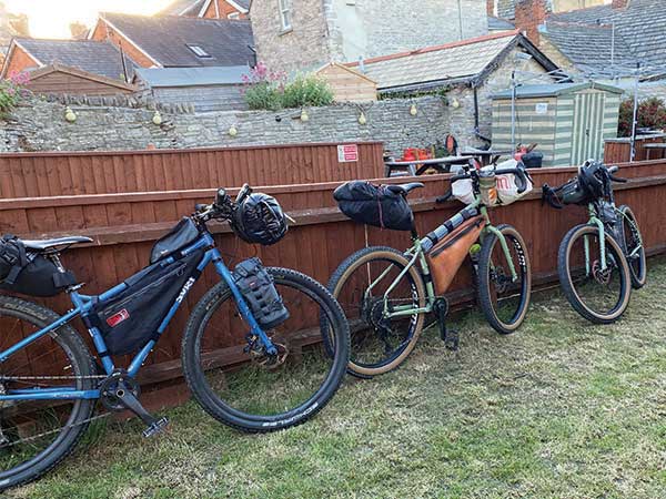 Three loaded bikes parked along wooden fence outside pub