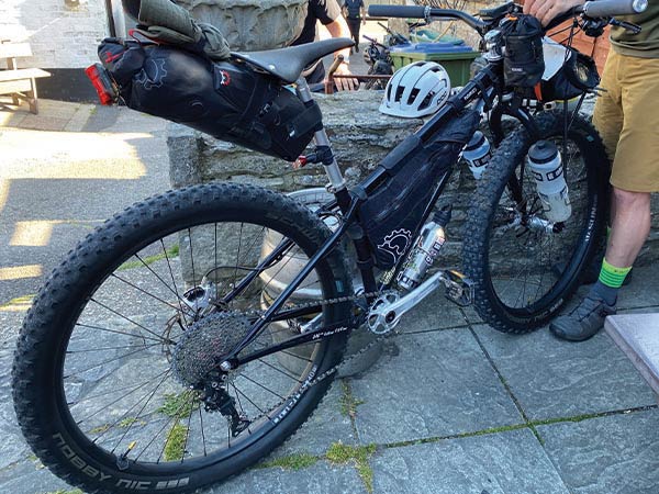 Person holding up black Surly mountain bike with three big water bottles, seatpack, frame bag, outside pub