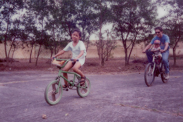 Aneka as child riding green BMX bike, dad and little brother riding behind