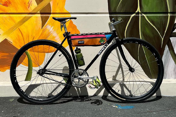 Black Surly Steamroller with flat bar, half frame pack, and water bottle and cage, leaning against building outside