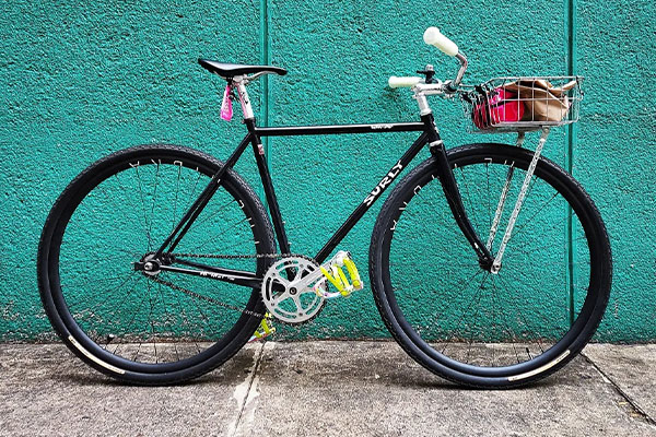 Black Surly Steamroller with cruiser bar and front basket rack leaning against wall outside