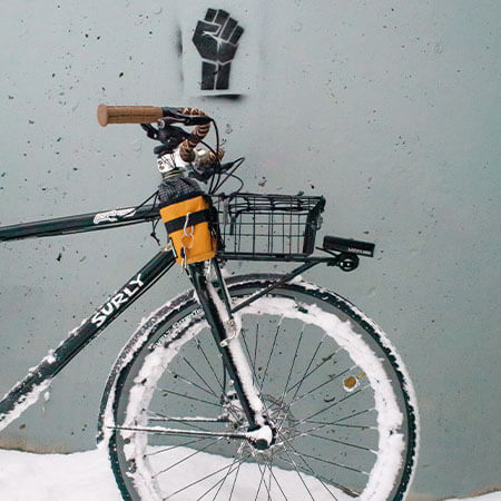 Surly Bridge Club, front end of bike parked against building with spray painted fist, in snow, packed on front wheel