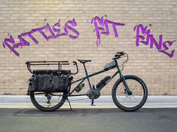 Side view of Abner's custome Big Easy, parked with kickstand down in front of brick building, graffiti 'Fatties Fit Fine'