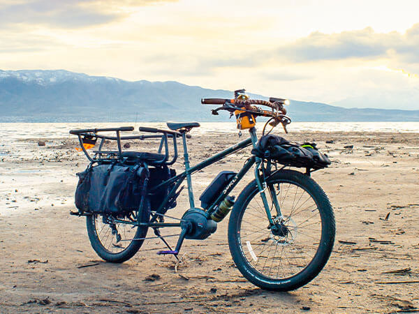 Surly Big Easy with front rack and bag, Kid Corral seat and bars, kickstand down on sandy beach, mountains in background