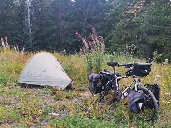 Small tent pitched in tall grass with loaded Troll bike parked