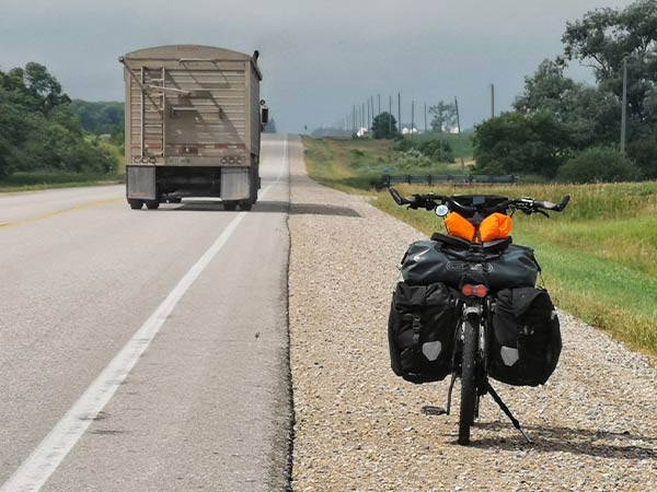 Troll bike loaded and parked on gravel shoulder of paved road as semi truck passes
