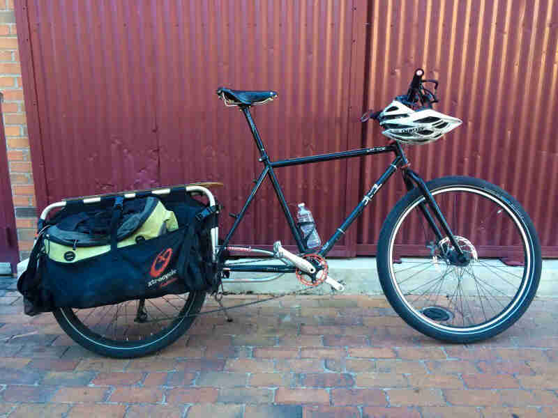 Right side of a green bike with rear rack and saddlebags, parked next to a red wall