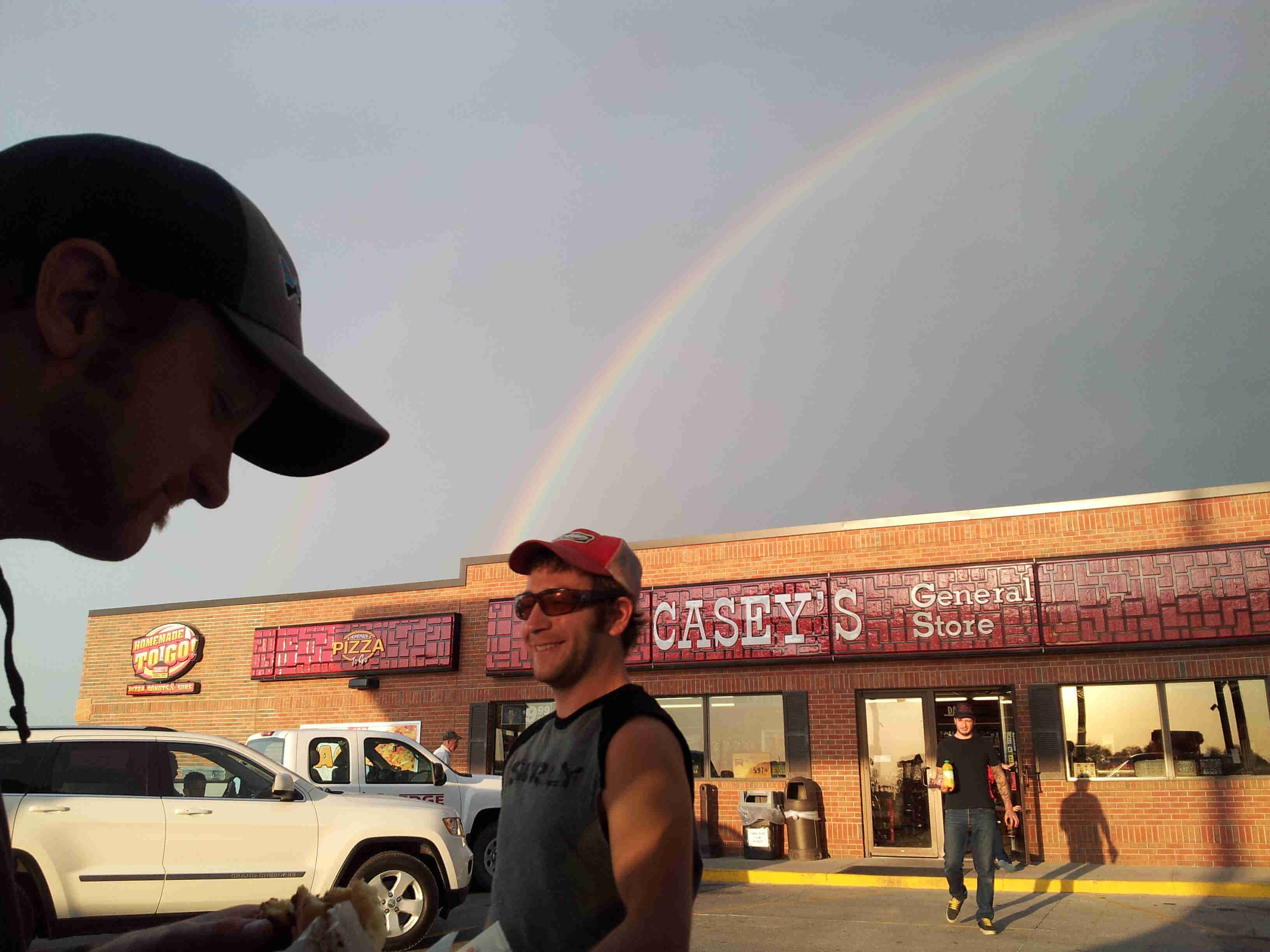Front view of people outside of a CASEY's general store, with a rainbow arching over