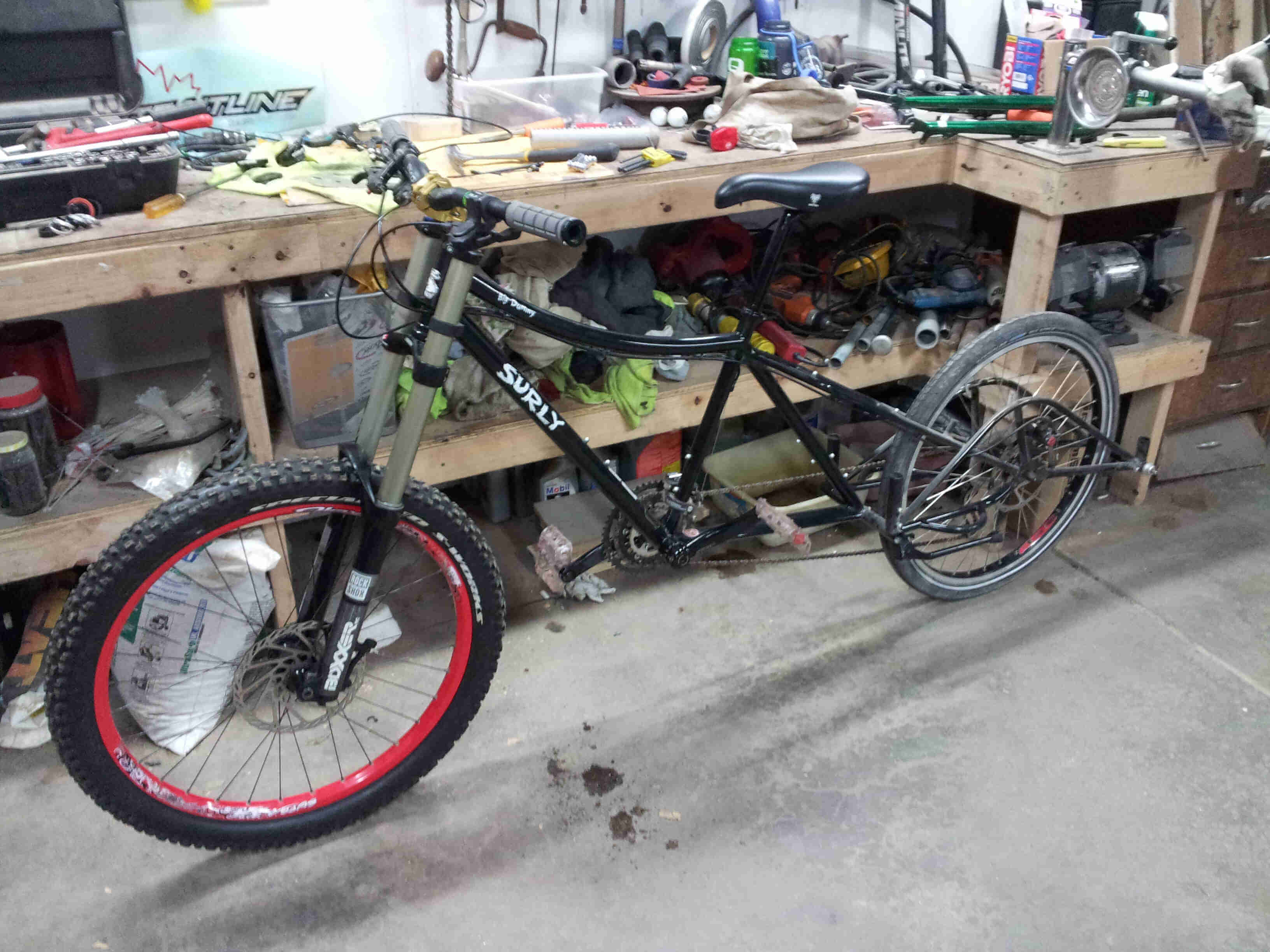 Left side view of a black Surly Big Dummy bike, parked on concrete, alongside a workbench inside a workshop