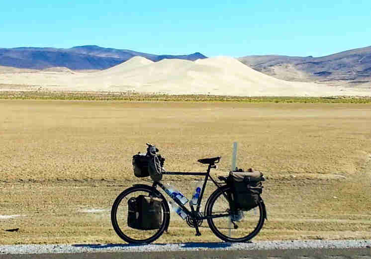 Left profile of a Surly bike, loaded with gear, parked on a roadside, with salt flats and mountains in the background