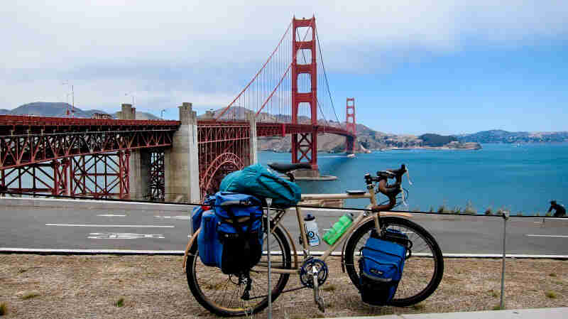 Right profile of a bike, loaded with gear, parked on a roadside, with the Golden Gate bridge and bay in the background