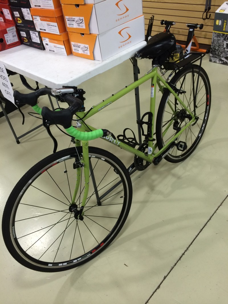 Left side view of a lime Surly Cross Check bike, leaning against a table with biking shoes on top, inside a bike shop