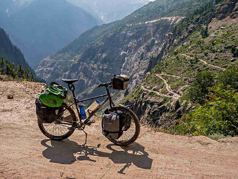 Right side view of a Surly Troll bike on a gravel road with a steep ledge, in the mountains