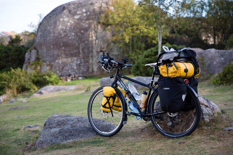 Left side view of a black Surly Ogre bike with gear, in a grass area with rocks, and a big stone mound in the background