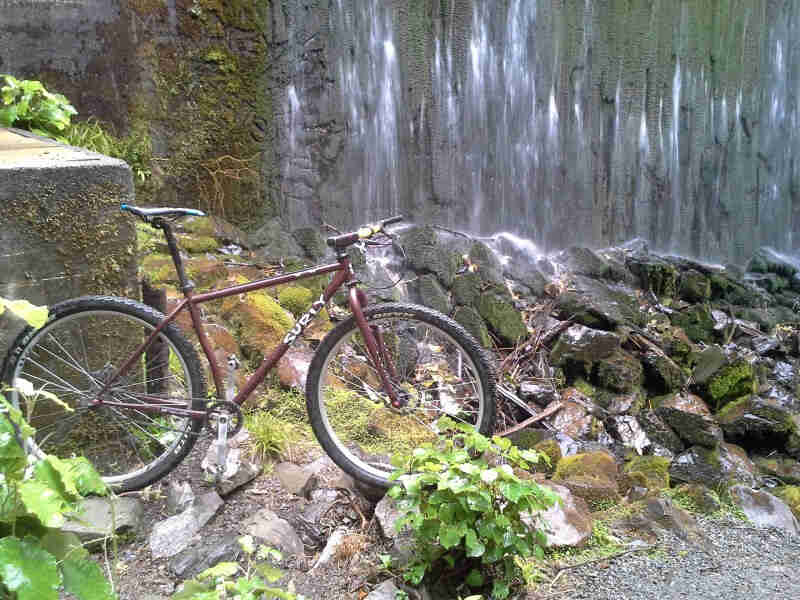 Right side view of a brown Surly bike, standing on rocks, with a stone cliff wall in the background