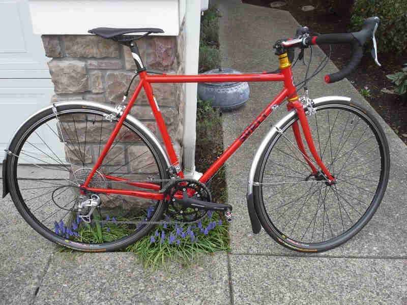Right side view of a red Surly bike, parked on a block walkway, leaning on the corner of a house
