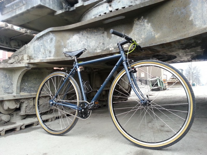 Right side view of a teal Surly bike, parked on concrete, and leaning against a large steel structure