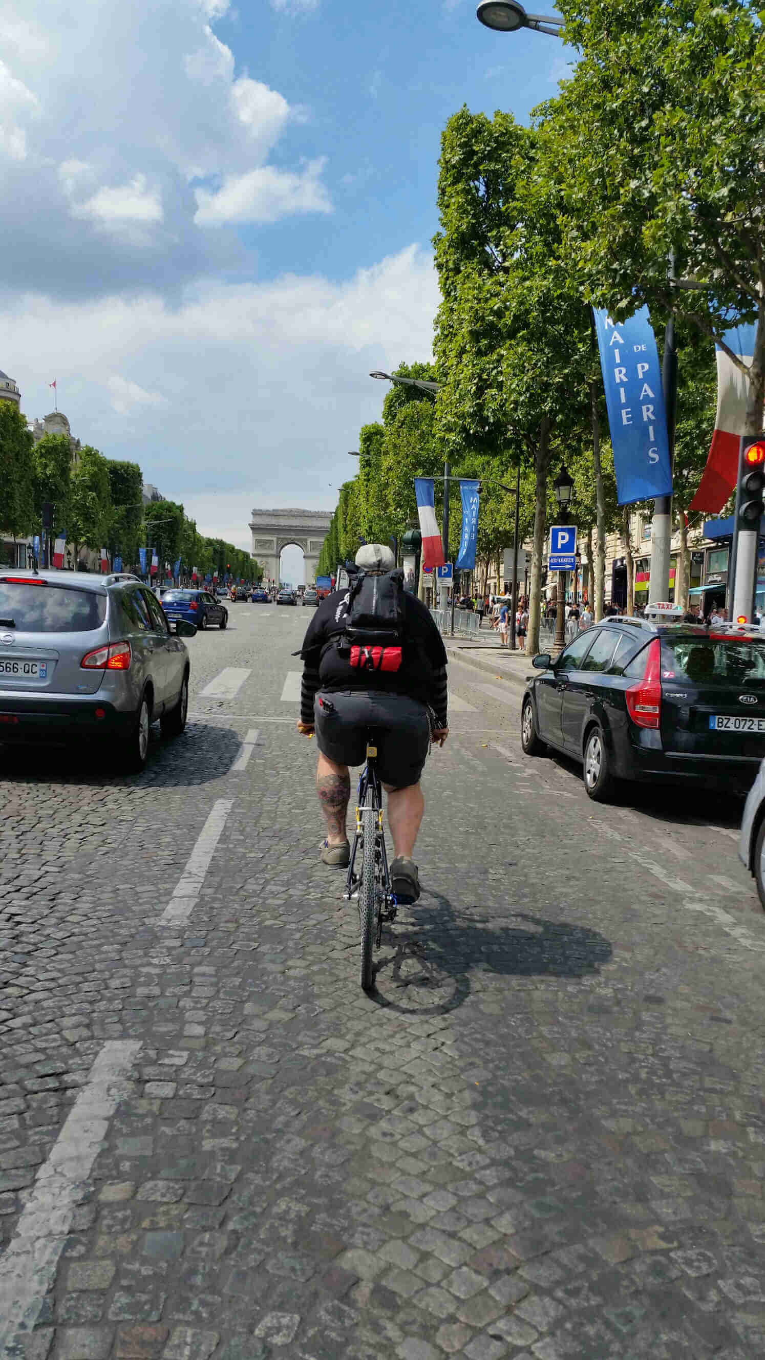 Rear view of a cyclist riding their bike on a street with cars, towards the Arc de Triomphe in Paris