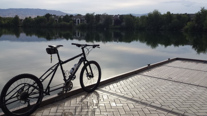 Right side view of a Surly Big Dummy bike, at the side edge of a dock with a brick deck, on a pond with trees behind