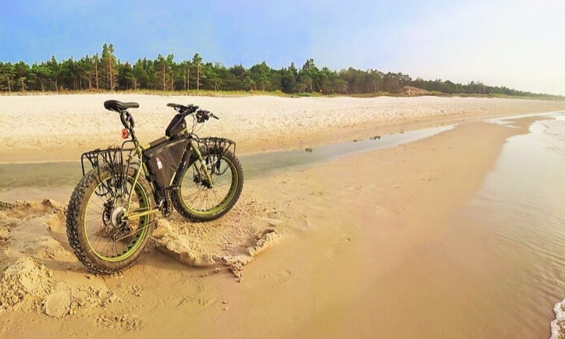 Right side view of a green Surly fat bike with a frame pack, parked on a beach with trees in the background