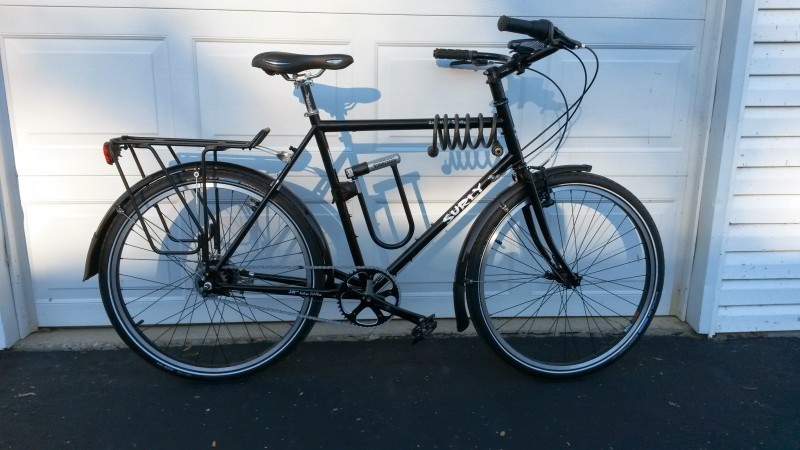 Right side view of a black Surly Long Haul Trucker bike with locks on it, leaning on the outside of a garage door