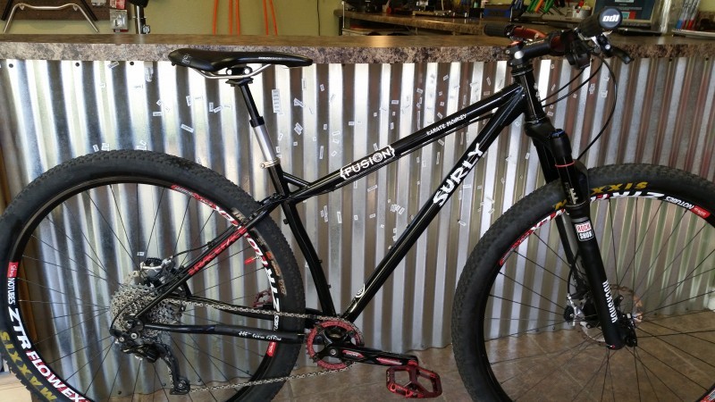 Right side view of a black Surly Karate Monkey bike, leaning against a corrugated steel wall, below a bar countertop