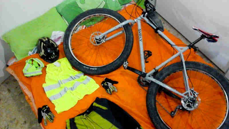 Downward view of a gray Surly bike, laying on it's right side in a bed, with reflective clothing laid out