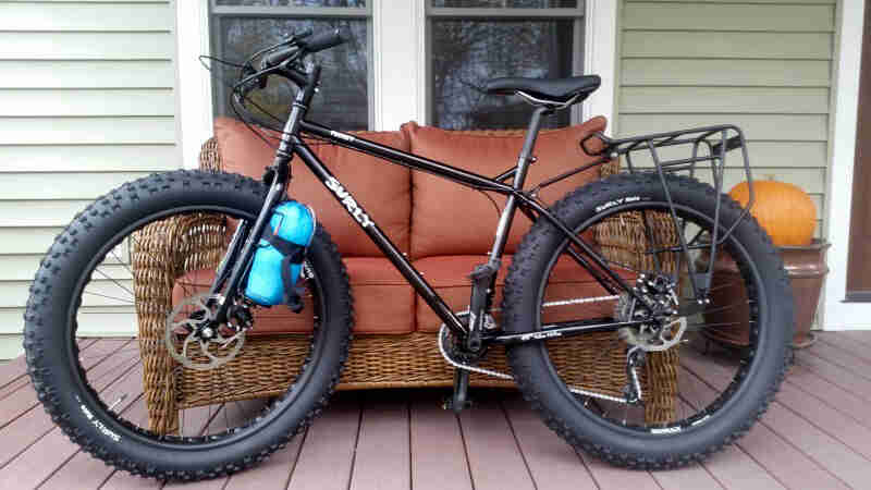 Left side view of a black Surly Pugsley fat bike, parked against a couch on an outdoor house porch