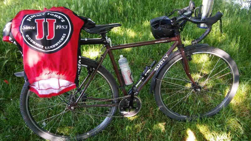 Right side view of a brown Surly bike with a Jimmy Johns bike jersey on the seat, parked on grass