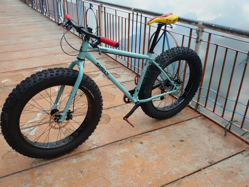 Left side view of a Surly Wednesday MY17 fat bike, mint, parked across a bridge, with the back wheel against the rail