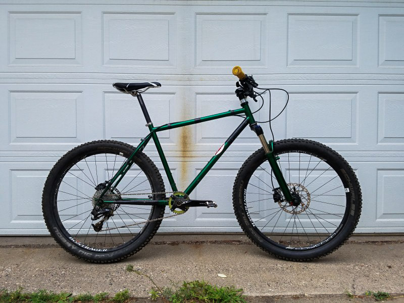 Right profile of a Surly bike, green, parked on cement in front of a garage door