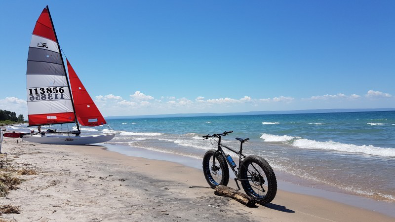 Rear view of a Surly fat bike, parked along a beach, with a sailboat ahead in the sand
