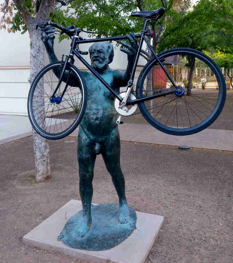 A black Surly bike set in the outreached hands of a statue of a man