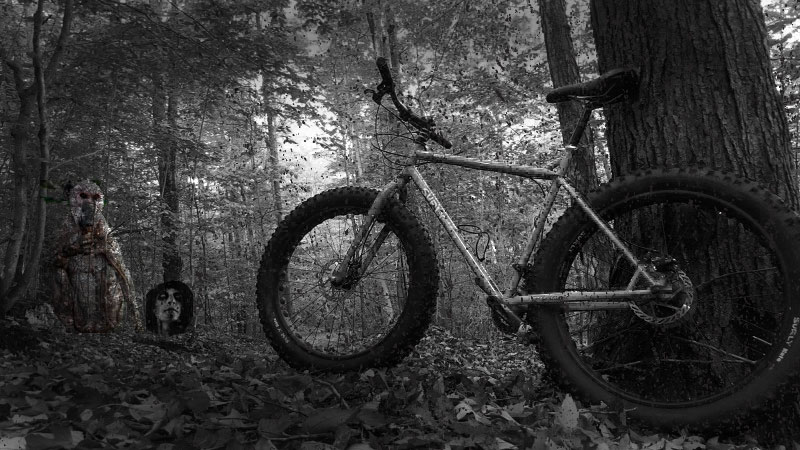 Left side view of a Surly fat bike parked in the forest, with faint ghostly figures in front - black & white images
