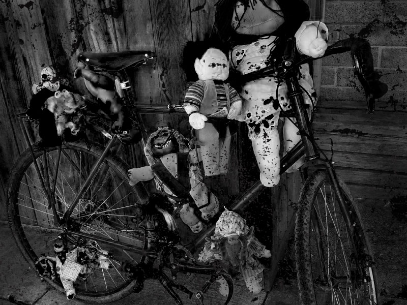 Right side view of a Surly bike covered in scary dolls, parked in front of a wall - black & white image