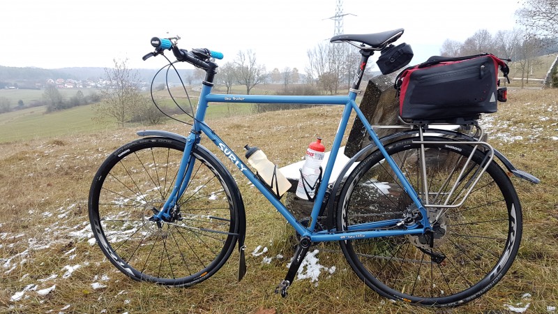 Left profile of a Surly Disc Trucker bike, next to a park bench, on a hill with snow patches