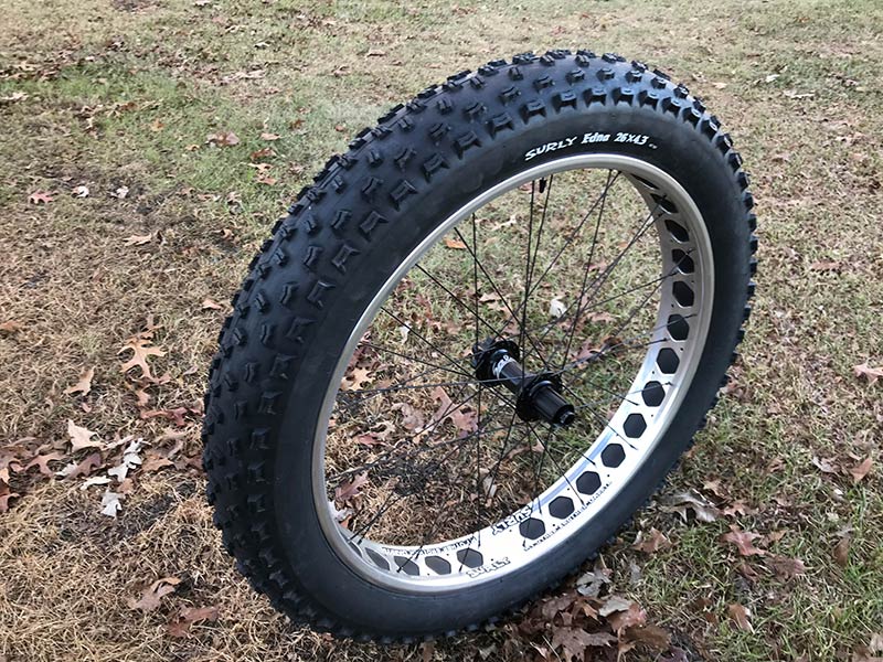 Angled, side profile view of a Surly fat bike wheel assembly with a Edna tire, standing in grass