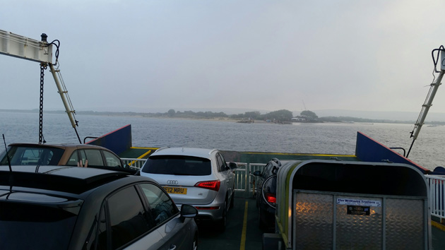 Front of a ferry with vehicles facing towards land on a cloudy day
