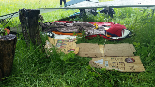 Boots and gear laying in the grass underneath an slightly elevated gray tarp