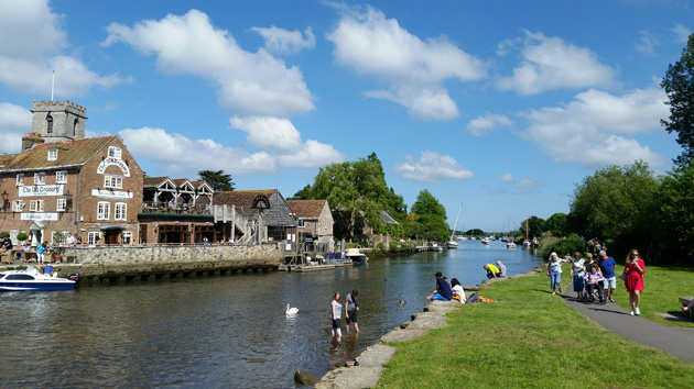 People gathering in and around a canal lined with buildings and blue sky with clouds in the background