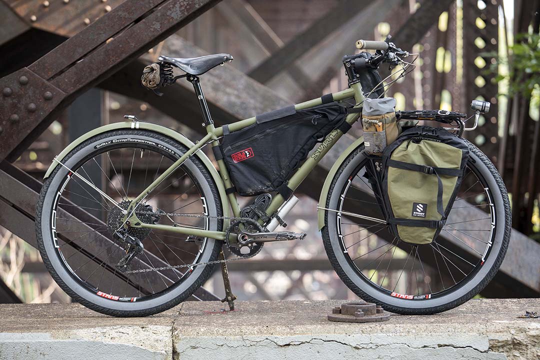 Right side view of an olive drab Surly Bridge Club bike with a front saddle bag, on a rusty steel bridge
